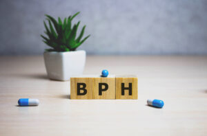 Wooden blocks featuring the letters BPH on a table with blue pills and a potted plant